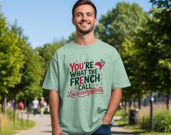 Puede incluir: Una camiseta verde claro con el texto "You're what the French call Les incompetents" en rojo y blanco. La camiseta tiene un gorro de Papá Noel y un gráfico de muérdago. La persona lleva vaqueros azules.