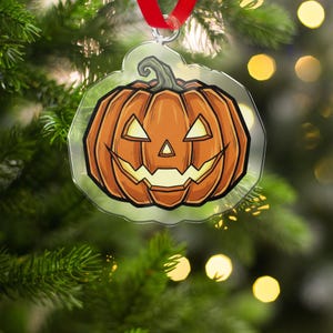 Op de afbeelding: Een heldere, pompoenvormige ornament met een lachend jack-o'-lantern ontwerp. De oranje pompoen heeft een zwarte omtrek en wordt opgehangen met een rood lint, perfect voor Halloween.