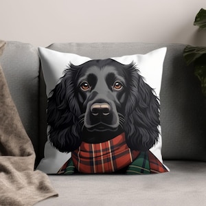 Può includere: Un cuscino decorativo con un'illustrazione dettagliata di un cane nero con occhi marroni. Il cane indossa una sciarpa a quadri rossa e verde. Il cuscino è su un divano grigio.