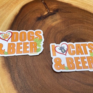 May include: Two stickers with orange text on a white background. One says "I ❤️ DOGS & BEER" with a paw print in a heart. The other says "I ❤️ CATS & BEER" with a cat in a heart. Both have hop illustrations.