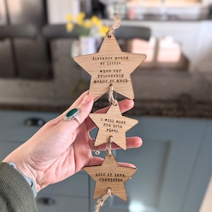 May include: A wooden star garland with three stars hanging from a string. The stars have messages written on them, including "distance means so little, when our friendship means so much." and "lots of love, charlotte".