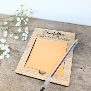 May include: A wooden notepad with a sticky note and a pen. The notepad has the text "Charlotte's things to remember" engraved on it.
