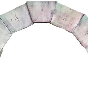 May include: A stone archway made of nine rectangular blocks, each with a number painted on it. The blocks are arranged in a semi-circle shape, with the top block being number 5. The blocks are painted in shades of gray, white, and pink.