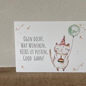 Könnte beinhalten: Eine weiße Geburtstagskarte mit einer Aquarellillustration einer Katze mit Partyhut und Geburtstagskuchen. Die Katze hält auch einen grünen Ballon. Die Karte hat Text auf Niederländisch.