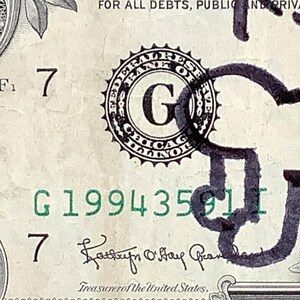 K&ouml;nnte beinhalten: Nahaufnahme einer Ein-Dollar-Note mit dem Text "THIS NOTE IS LEGAL TENDER" und der Seriennummer G19943591I. Die Note zeigt ein Federal Reserve Siegel und die Unterschrift des Schatzmeisters der Vereinigten Staaten.