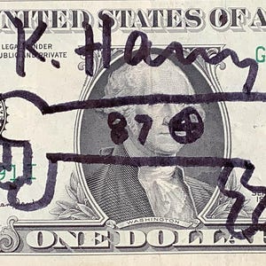 K&ouml;nnte beinhalten: Ein Ein-Dollar-Schein mit einer schwarzen Markierung &uuml;ber dem Portr&auml;t von George Washington. Die Zeichnung enth&auml;lt den Namen "K. Harry" und die Zahl "87" mit einem Smiley. Der Text der Rechnung ist teilweise sichtbar.