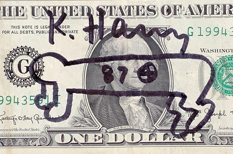 K&ouml;nnte beinhalten: Ein Ein-Dollar-Schein mit einer schwarzen Markierung &uuml;ber dem Portr&auml;t von George Washington. Die Zeichnung enth&auml;lt den Namen "K. Harry" und die Zahl "87" mit einem Smiley. Der Text der Rechnung ist teilweise sichtbar.