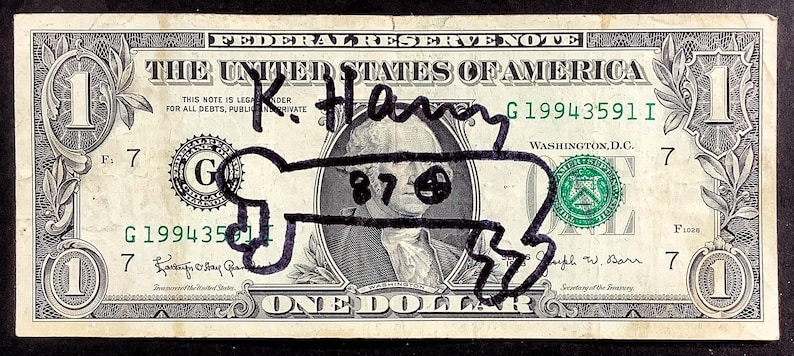 K&ouml;nnte beinhalten: Ein Ein-Dollar-Schein mit einer schwarzen Markierung, die eine Knochenform &uuml;ber dem Portr&auml;t von George Washington darstellt. Auf der Rechnung steht mit schwarzem Marker "K. Hany". Die Seriennummer der Rechnung lautet G19943591I.