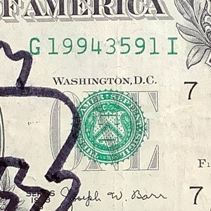 K&ouml;nnte beinhalten: Nahaufnahme eines Ein-Dollar-Scheins mit dem Wort "AMERICA" oben. Die Seriennummer "G19943591 I" ist sichtbar. Der Schein hat ein gr&uuml;nes Siegel und den Text "WASHINGTON, D.C."