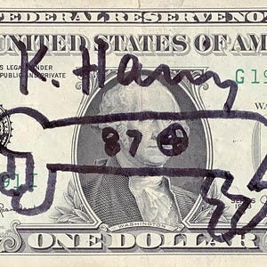 K&ouml;nnte beinhalten: Ein Ein-Dollar-Schein mit schwarzen Markierungen &uuml;ber dem Portr&auml;t von George Washington. Die Zeichnungen enthalten den Namen "K. Harry" und ein cartoonartiges Gesicht &uuml;ber Washingtons Gesicht. Der Text der Rechnung ist sichtbar.
