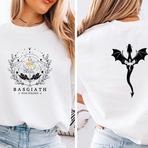 May include: White sweatshirt with a front graphic that reads "BASGIATH WAR COLLEGE" and a detailed design of a sword, wings, and floral elements. The back features a black dragon silhouette.
