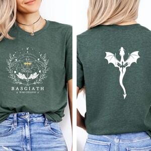 May include: Green t-shirt with a white graphic on the front and back. The front features the text "BASGIATH WAR COLLEGE" with a detailed emblem. The back displays a white dragon design. The shirt is made of a soft material.