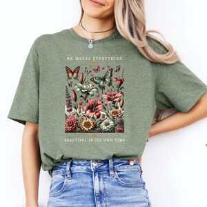 Op de afbeelding: Groen T-shirt met een bloemenontwerp en vlinders. De tekst "He makes everything beautiful in its own time" staat op het shirt gedrukt.