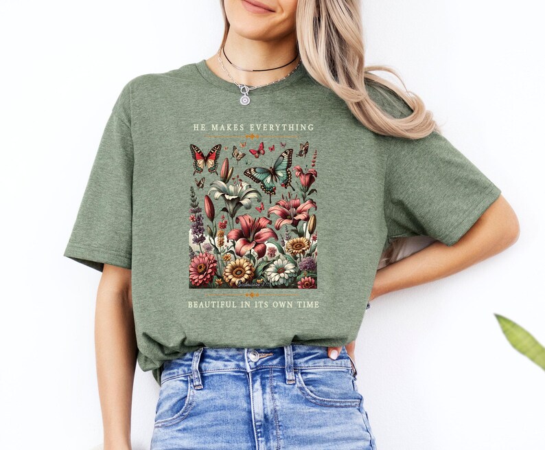 Op de afbeelding: Groen T-shirt met een bloemenontwerp en vlinders. De tekst "He makes everything beautiful in its own time" staat op het shirt gedrukt.