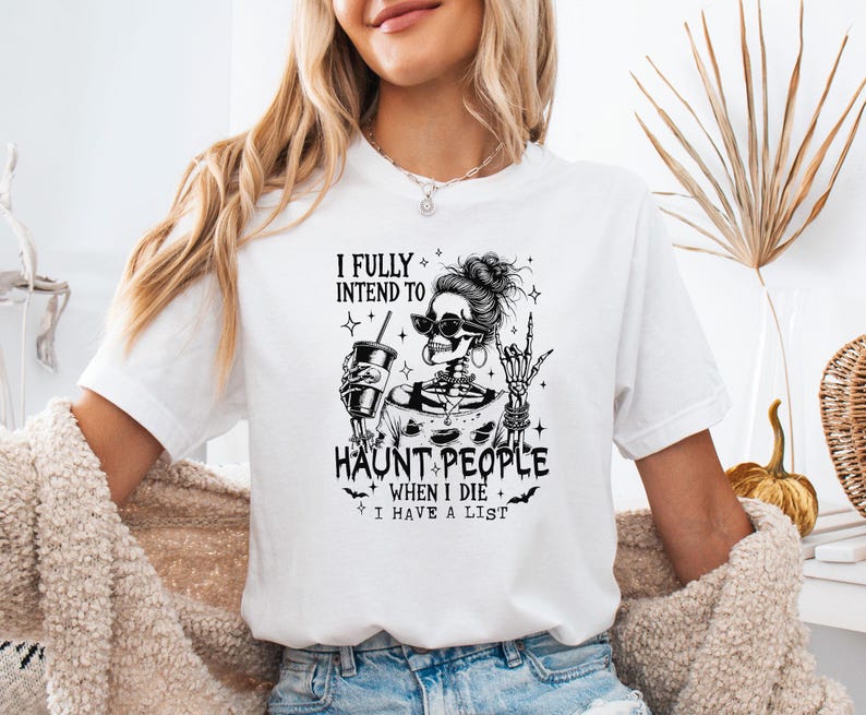 May include: White t-shirt with a black graphic of a skeleton wearing sunglasses and holding a drink. The text reads "I FULLY INTEND TO HAUNT PEOPLE WHEN I DIE I HAVE A LIST."