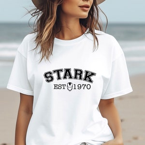 May include: White t-shirt with black text that reads "STARK EST 1970" with a small iron man logo in between the words.