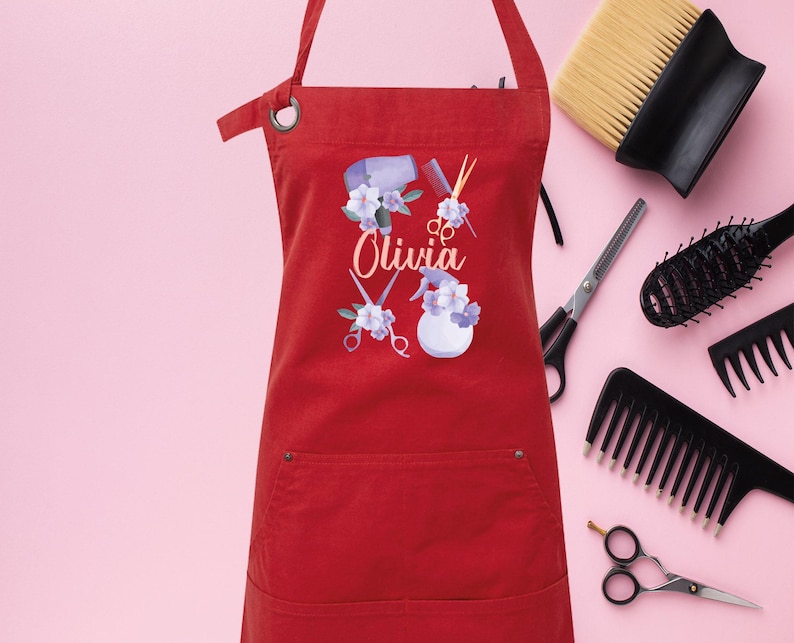 May include: Red apron with a pocket, featuring a design of hairdressing tools, flowers, and the name "Olivia".