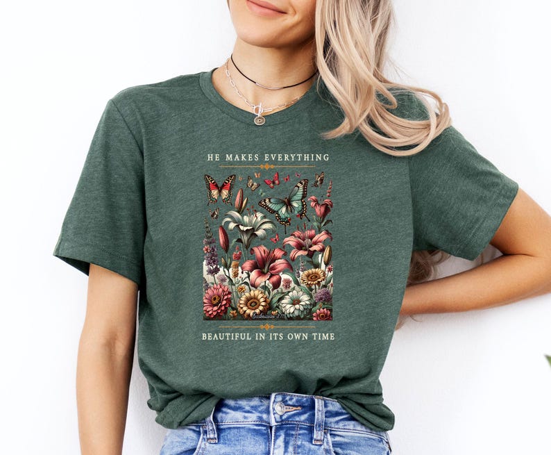 Op de afbeelding: Een groen T-shirt met een bloemenpatroon en vlinders. De tekst "He makes everything beautiful in its own time" staat op het shirt gedrukt.