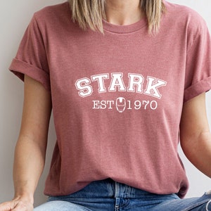 May include: A maroon t-shirt with white text that reads "STARK EST 1970" with an iron man symbol in between the words "EST" and "1970".