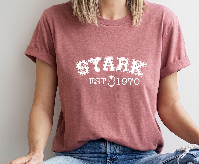 May include: A maroon t-shirt with white text that reads "STARK EST 1970" with an iron man symbol in between the words "EST" and "1970".