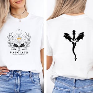 May include: White t-shirt featuring a black and gold graphic on the front with the text "BASGIATH WAR COLLEGE". The back of the shirt displays a black dragon silhouette. The shirt is made of a soft material.