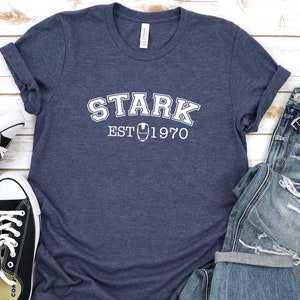 May include: A navy blue t-shirt with white text that reads "STARK EST 1970" and a small iron man symbol.