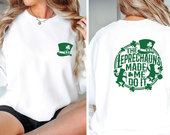 May include: A white crewneck sweatshirt featuring a small green leprechaun hat graphic on the front left chest. The back displays a large circular green graphic with leprechaun silhouettes, shamrocks, and the text THE LEPRECHAUNS MADE ME DO IT.