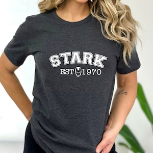 May include: A dark gray t-shirt with white text that reads "STARK EST 1970" with a stylized iron man mask in between the words "EST" and "1970".