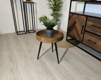 May include: A small, round wooden side table with a tray-like top and three black metal legs. A small potted plant sits on the table. Other furniture includes a cabinet and two tall, black metal stands.