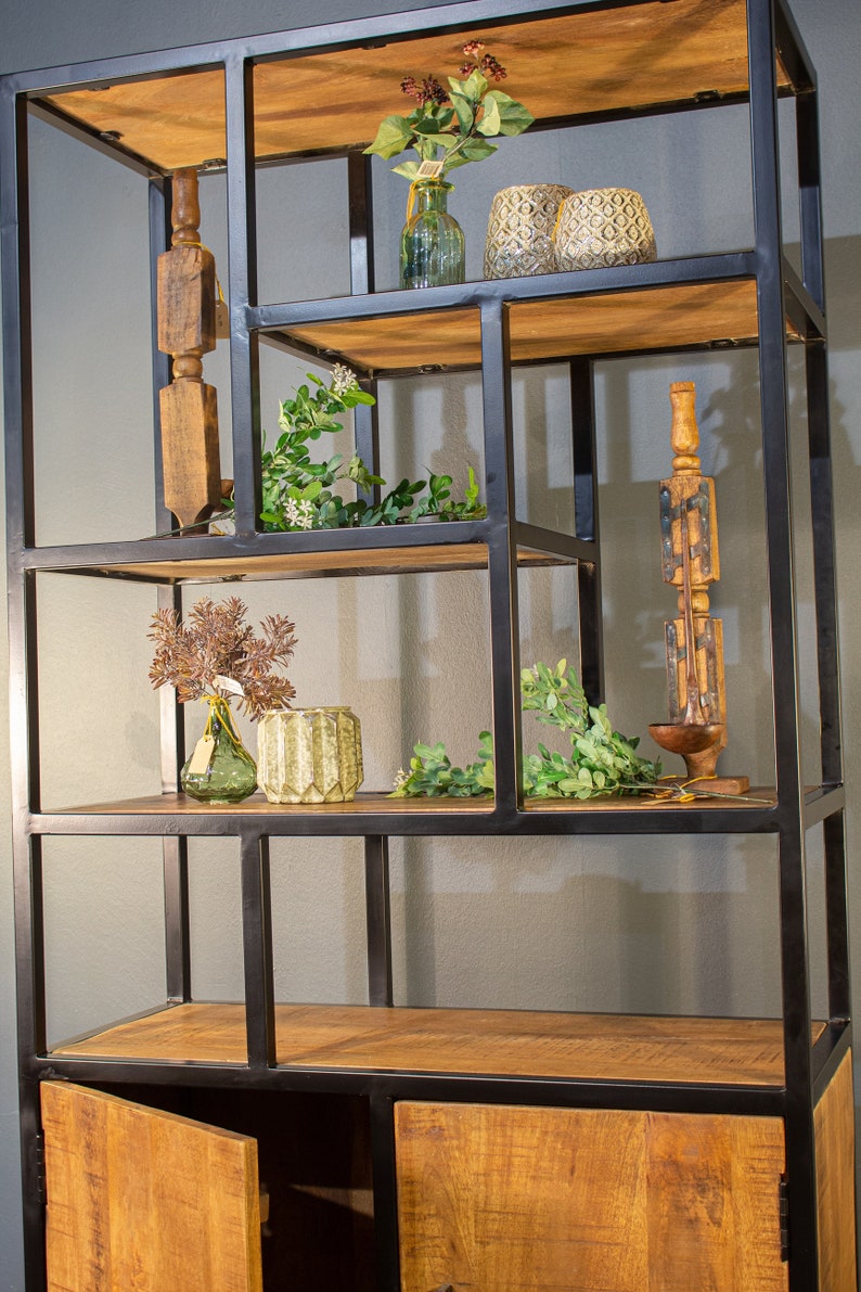 May include: A black metal shelf unit with wooden shelves and a cabinet with two doors. The shelves are decorated with plants, vases, and decorative items.
