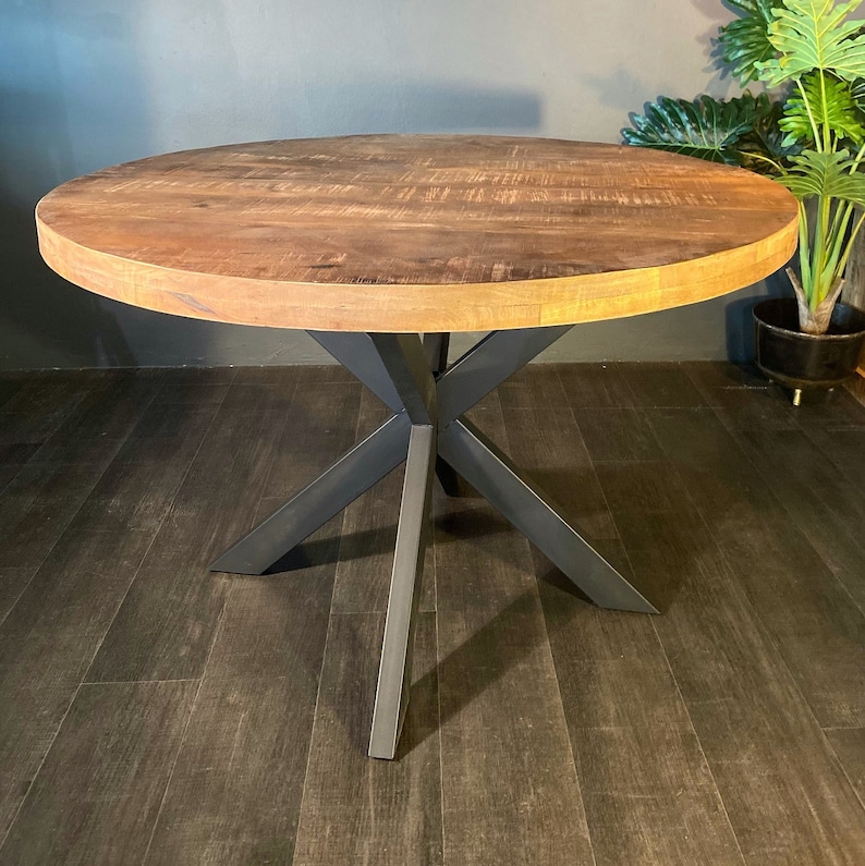 May include: A round wooden table with a black metal base. The table top has a natural wood grain finish. The base is made of four legs that are connected in the middle.