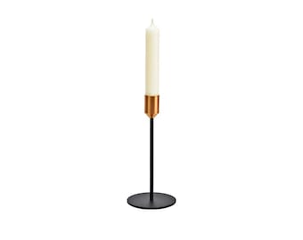 May include: A black metal candle holder with a gold top and a white candle. The holder has a round base.
