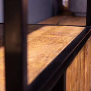 May include: Close-up of a wooden shelf with a black metal frame. The shelf is made of natural wood with a warm brown color. The metal frame is black and has a sleek, modern design.