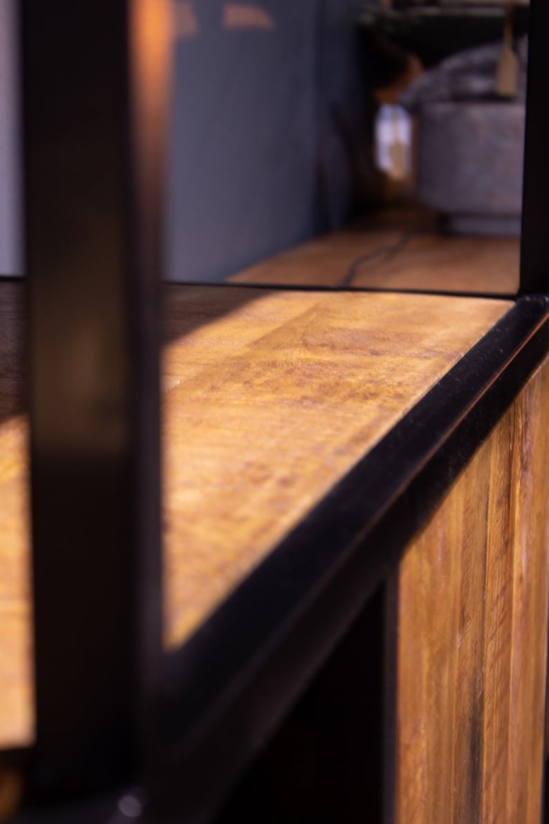 May include: Close-up of a wooden shelf with a black metal frame. The shelf is made of natural wood with a warm brown color. The metal frame is black and has a sleek, modern design.