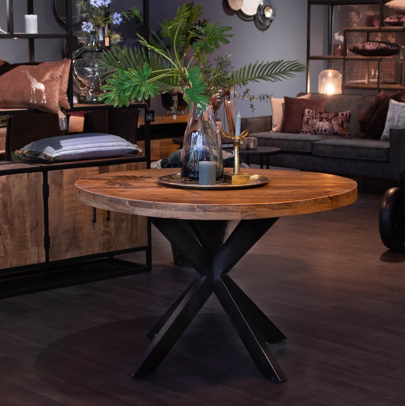 May include: A round wooden table with a black X-shaped base. The table has a natural wood finish and is decorated with a tray of greenery, candles, and a gold deer figurine.