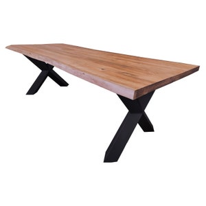 Op de afbeelding: Een lange, houten eettafel met een natuurlijke houtkleur en een levende rand. De tafel heeft een zwart metalen X-vormig onderstel.