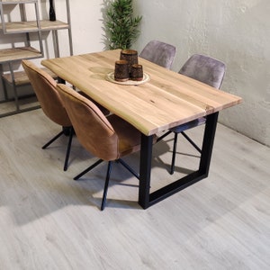 Puede incluir: Una mesa de comedor de madera con una tapa de borde vivo y patas de metal negro. La mesa está puesta con cuatro sillas, dos con tapicería marrón y dos con tapicería gris. Hay tres candelabros decorativos en la mesa.