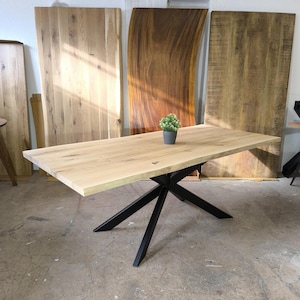 Könnte beinhalten: Ein großer Esstisch aus Holz mit einer Live-Edge-Platte und einem schwarzen X-förmigen Metallgestell. Der Tisch ist aus hellem Holz und hat eine natürliche Oberfläche. Das Gestell ist aus robustem Metall und hat eine schwarze Pulverbeschichtung.