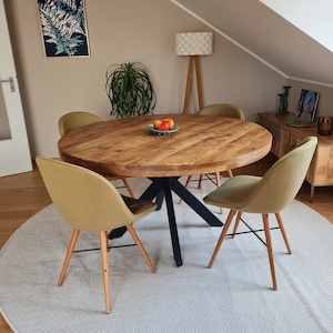 May include: A round wooden dining table with a black metal base and four light green chairs. The table is set with a bowl of fruit and a white rug is under the table.