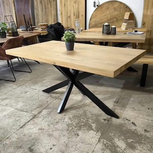 Könnte beinhalten: Ein rechteckiger Esstisch aus Holz mit einer natürlichen Holzoptik und einem schwarzen X-förmigen Metallgestell.