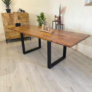 Op de afbeelding: Een houten eettafel met een natuurlijke houten afwerking en zwarte metalen poten. De tafel heeft een blad dat kan worden uitgeklapt om hem langer te maken. De tafel is gedekt met een klein dienblad met decoratieve items.