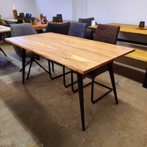 Könnte beinhalten: Ein Esstisch aus Holz mit einer Tischplatte aus lebender Kante und schwarzen Metallbeinen. Der Tisch ist von Stühlen mit gepolsterten Sitzen umgeben.