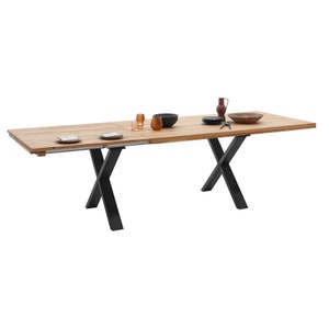 Op de afbeelding: Een houten eettafel met een natuurlijke afwerking en zwarte metalen X-vormige poten. De tafel heeft een blad dat kan worden uitgebreid om de lengte van de tafel te vergroten.