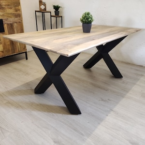 Könnte beinhalten: Ein Esstisch aus Holz mit einer hellbraunen Tischplatte und schwarzen X-förmigen Beinen. Der Tisch steht auf einem hellen Holzboden.