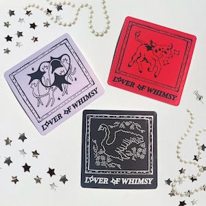 May include: Three square stickers featuring the text LOVER OF WHIMSY. One is light purple with a black illustration of star-like figures, one is red with a black illustration of a calf, and one is black with a white dotted illustration of a swan.