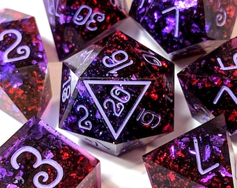 May include: A set of purple and red dice with white numbers and glitter embedded in the resin. The dice are in various shapes, including a d20, d12, d10, d8, d6, and d4.
