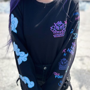 May include: Black long-sleeve shirt with a pixelated design featuring a crown, clouds, and the words "POW! POW!" and "HEEE!"