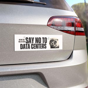May include: White rectangular bumper sticker with the text "OR MY CAT WILL BE SAD SAY NO TO DATA CENTERS" and a grayscale image of a cat. The sticker is affixed to the back of a silver car.
