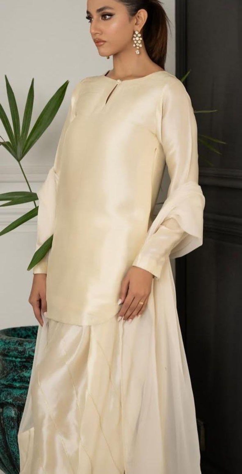 May include: A cream-colored, long-sleeved dress with a flowing skirt and a keyhole neckline. The dress is made of a silky fabric and has a subtle sheen.