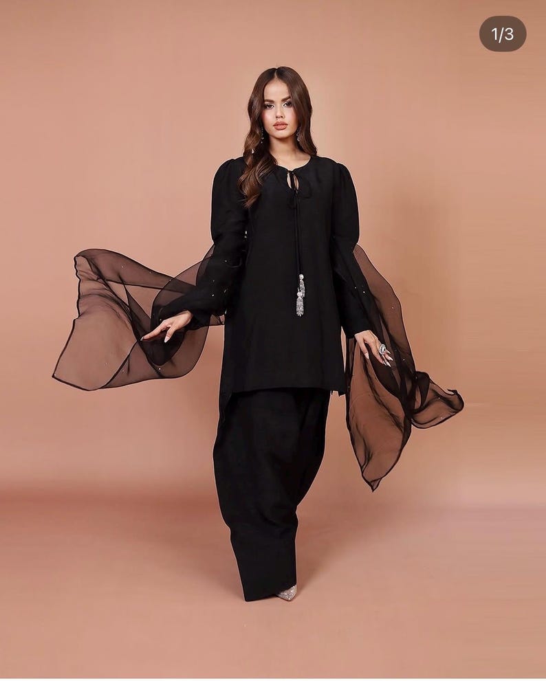 May include: A black long-sleeved tunic with a keyhole neckline and a tassel detail. The tunic is paired with black pants and a sheer black scarf.